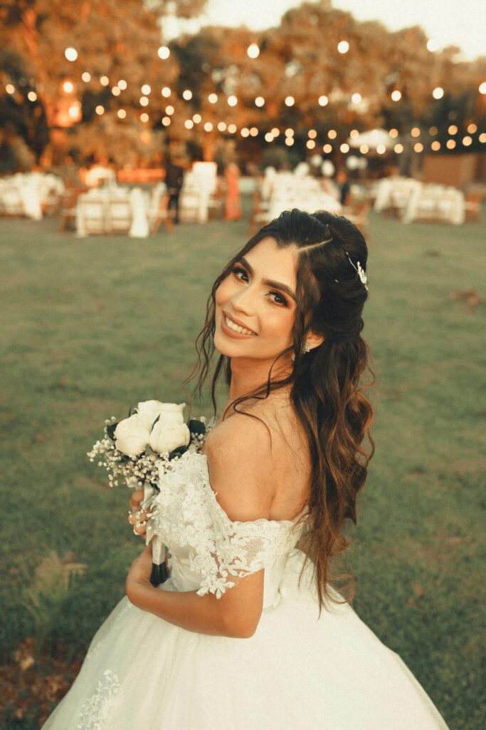 A happy bride embraces her wedding day with a bouquet in an outdoor setting, smiling brightly.